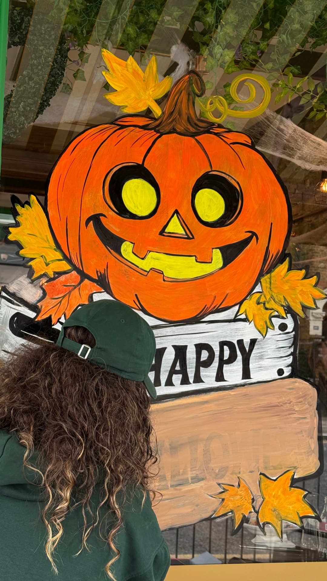 Jan Sel beside a hand-painted Happy Halloween pumpkin cafe window mural